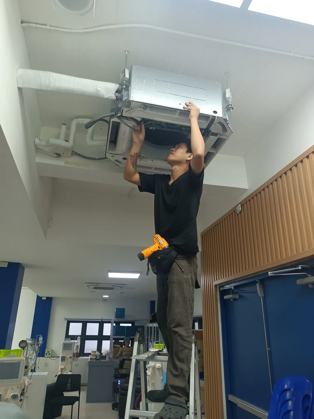 Wattsavers technician servicing a ceiling-cassette air-conditioning unit in a hospital ward